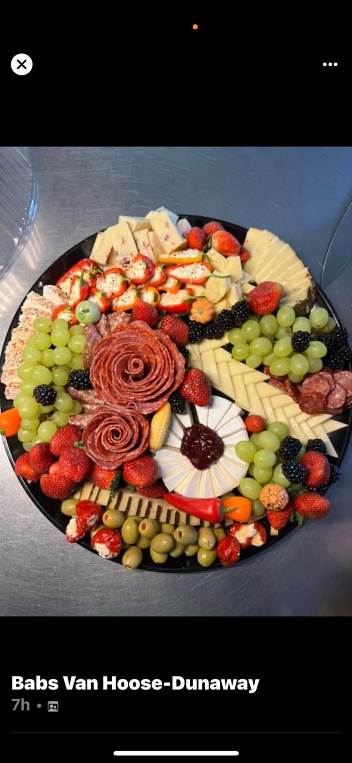 A colorful round platter of cheeses, meats, fruit, and olives.